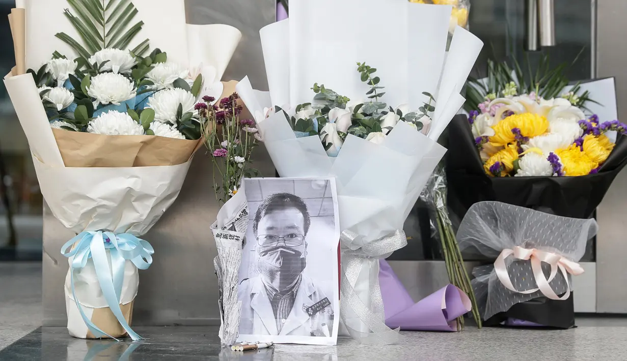 Karangan bunga dan foto mendiang dokter Li Wenliang terlihat di Cabang Houhu Rumah Sakit Pusat Wuhan di Wuhan di provinsi Hubei, China, Jumat, (7/2/2020). Li Wenliang sebelumnya memberikan peringatan kepada publik tentang potensi munculnya virus corona pada Desember 2019. (AFP/STR)