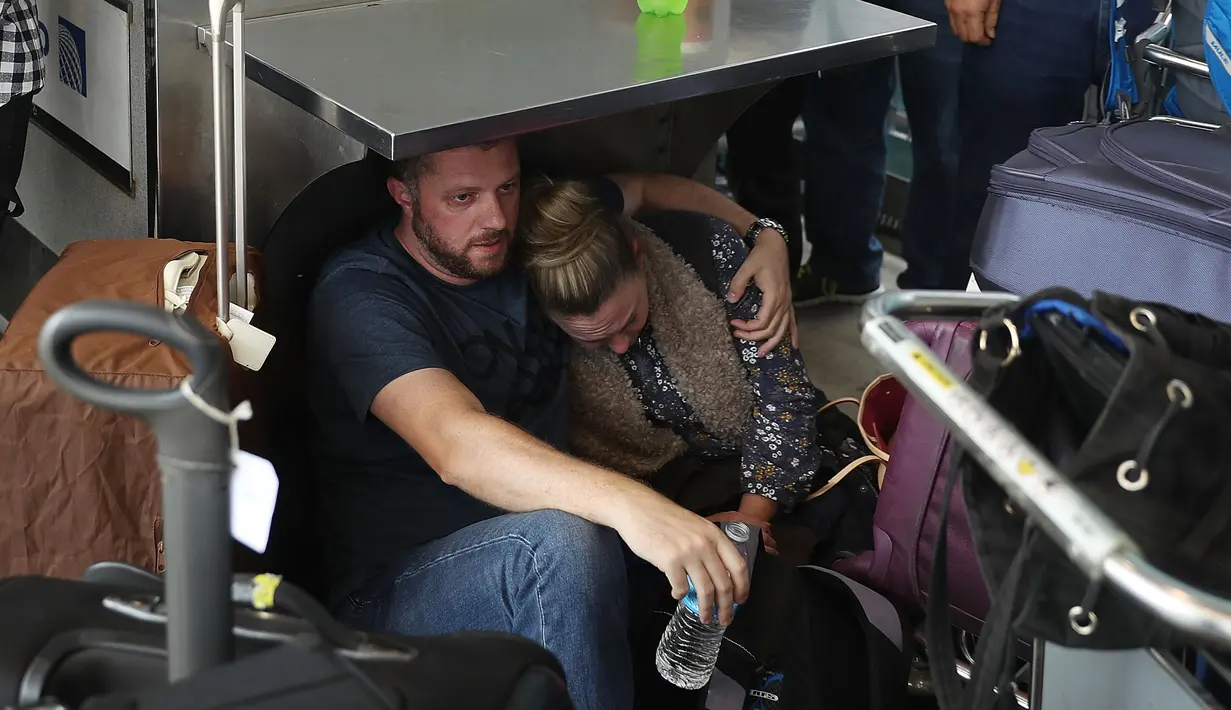 Dua penumpang berlindung saat terjadi penembakan di Bandara Fort Lauderdale, Florida, AS (6/1). Diketahui pelaku penembakan pernah bertugas di Irak selama setahun. (Joe Raedle/Getty Images/AFP Photo)