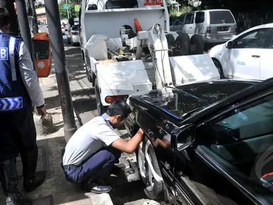 Petugas Dishub memasang alat derek pada kendaraan yang parkir liar di kawasan Cikini, Jakarta, Selasa (28/4/2015). Masih banyak mobil pribadi yang parkir disembarang tempat.(Liputan6.com/JohanTallo)