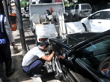 Petugas Dishub memasang alat derek pada kendaraan yang parkir liar di kawasan Cikini, Jakarta, Selasa (28/4/2015). Masih banyak mobil pribadi yang parkir disembarang tempat.(Liputan6.com/JohanTallo)