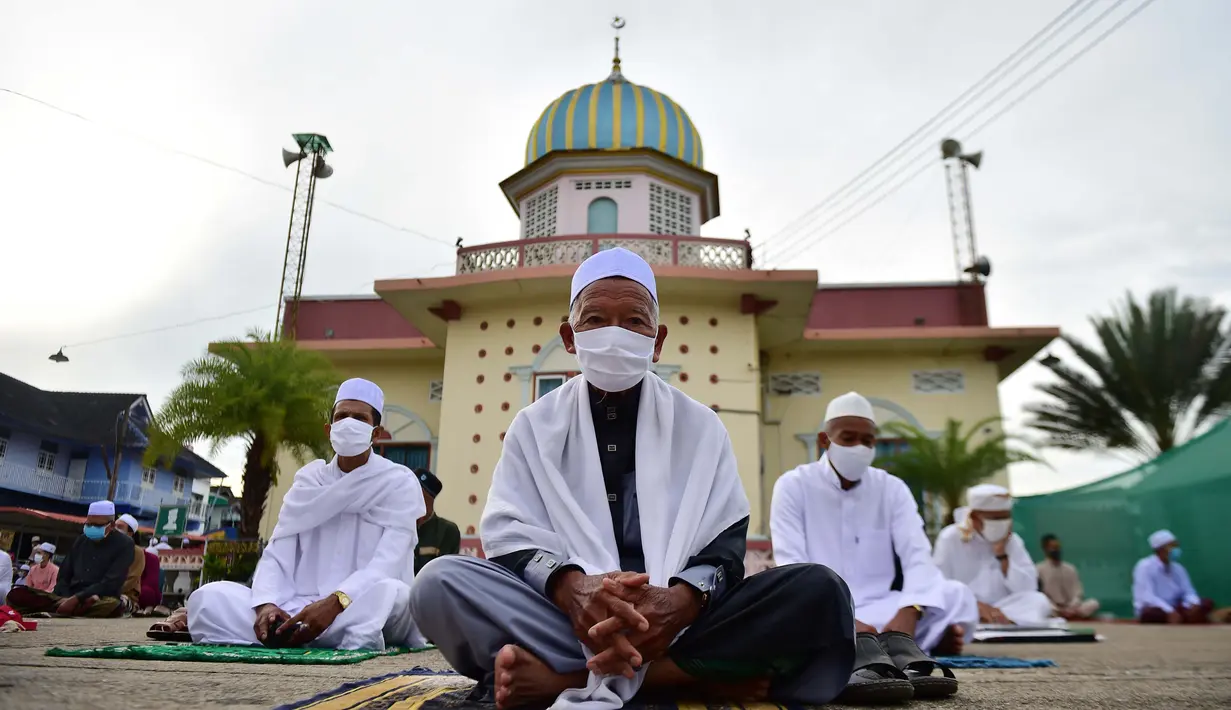 Pria-pria Muslim mengenakan masker dan duduk dengan menjaga jarak untuk melaksanakan salat berjemaah pada Idul Fitri yang menandai akhir bulan suci Ramadhandi halaman masjid Yakaniah di Narathiwat, provinsi selatan Thailand, 24 Mei 2020. (Photo by Madaree TOHLALA / AFP)