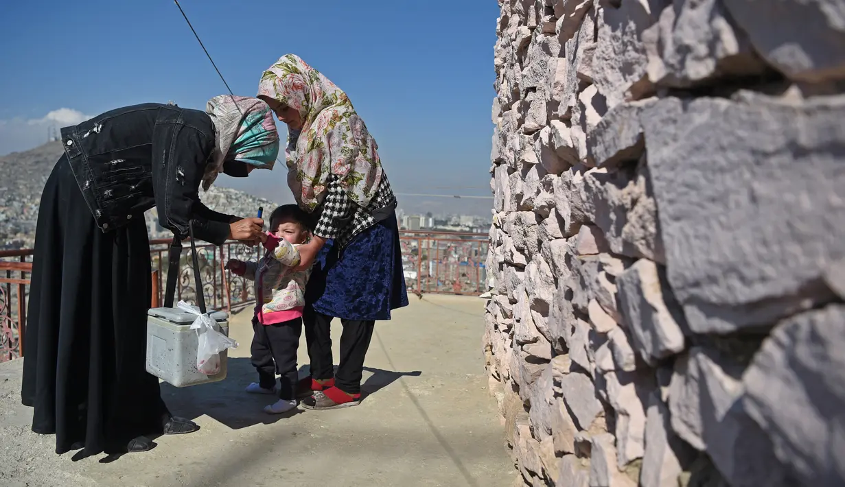 Tenaga kesehatan (kiri) memberikan vaksin polio kepada seorang anak selama kampanye vaksinasi di kawasan tua Kabul, Afghanistan pada 8 November 2021. Vaksinasi tersebut merupakan yang pertama sejak Taliban berkuasa di Afghanistan. (WAKIL KOHSAR / AFP)