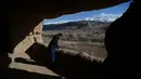 Seorang pria Hazara melihat keluar dari gua lokasi patung Buddha raksasa yang dihancurkan oleh Taliban pada 2001 di Provinsi Bamiyan, Afghanistan, 3 Maret 2021. Patung Buddha Bamiyan diukir pada tebing batu pasir di abad kelima silam. (WAKIL KOHSAR/AFP)