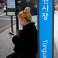 Seorang wanita bermain ponsel saat menunggu di halte bus di Seoul, Korea Selatan (19/2). (AFP Photo/David Gannon)