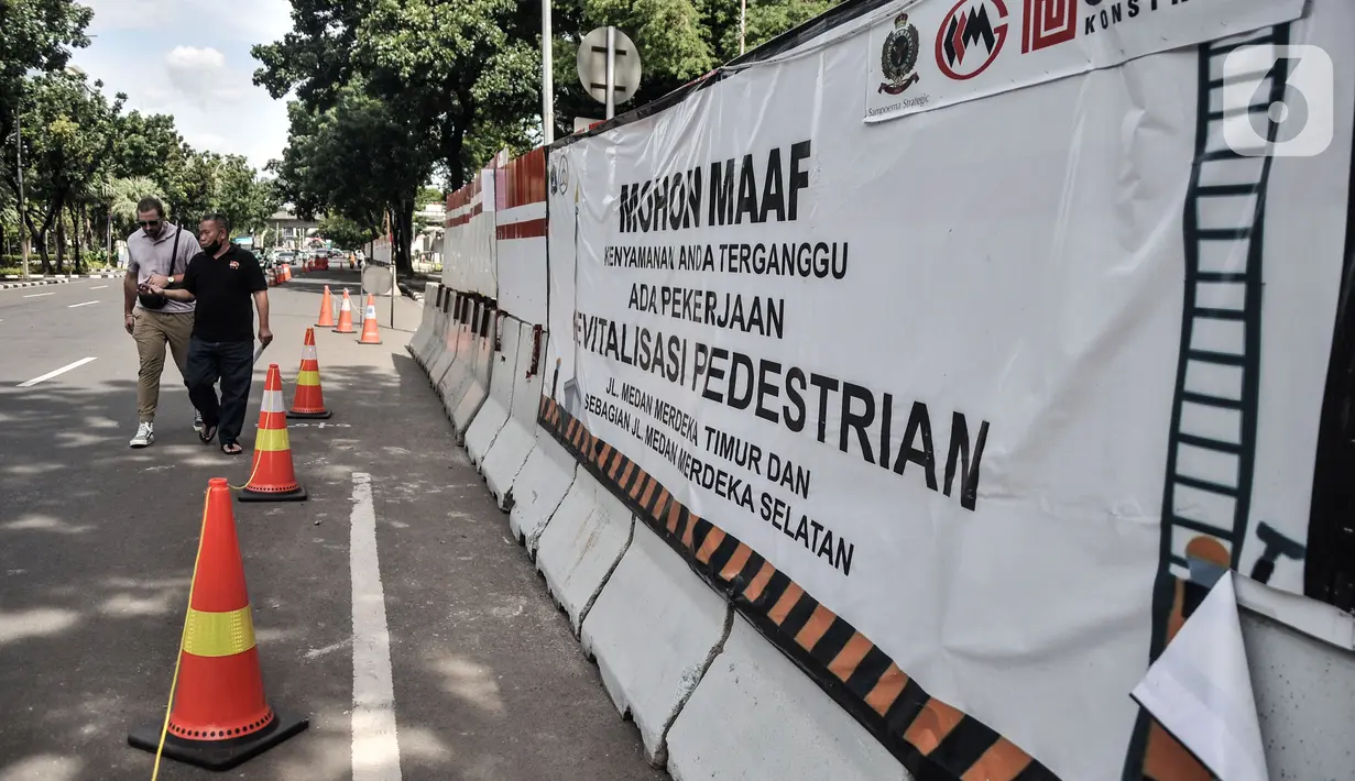 Pejalan kaki melintasi jalur sementara saat proyek revitalisasi trotoar di Jalan Medan Merdeka Selatan, Jakarta Pusat, Selasa (22/11/2022). Pemprov DKI Jakarta mengalokasikan anggaran sebesar Rp 171 miliar dalam Rancangan Anggaran Pendapatan dan Belanja Daerah (RAPBD) DKI Jakarta 2023 untuk revitalisasi trotoar di Ibu Kota. (merdeka.com/Iqbal S. Nugroho)