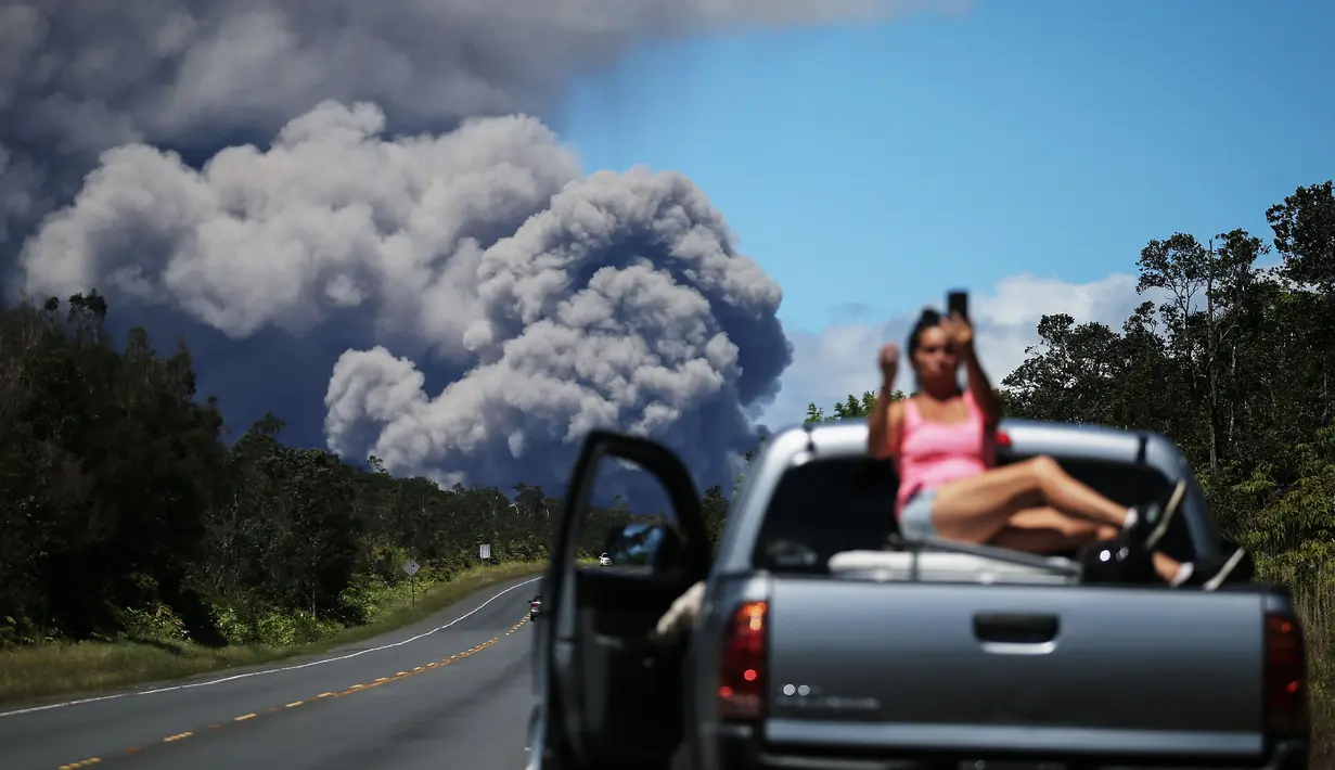 Seorang wanita berswafoto di atas mobil dengan latar belakang kepulan abu vulkanik dari gunung berapi Kilauea di Big Island Hawaii (15/5). Penduduk mendapat peringatan mengenai abu yang dapat menganggu pernapasan. (Mario Tama/Getty Images/AFP)