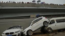 Orang-orang melihat mobil-mobil yang terendam banjir setelah hujan lebat melanda Zhengzhou di provinsi Henan, China, Kamis (22/7/2021). Curah hujan yang tinggi mengakibatkan aliran air sungai meluap ke jalan dan membuat sejumlah kendaraan terbawa arus dan bertumpuk di sudut jalan. (Noel Celis/AFP)