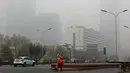 Petugas membersihkan jalanan saat diselimuti kabut asap tebal di Beijing, China (14/11). Pihak berwenang mengeluarkan peringatan kuning untuk polusi udara buruk pada hari Rabu. (AP Photo/Andy Wong)