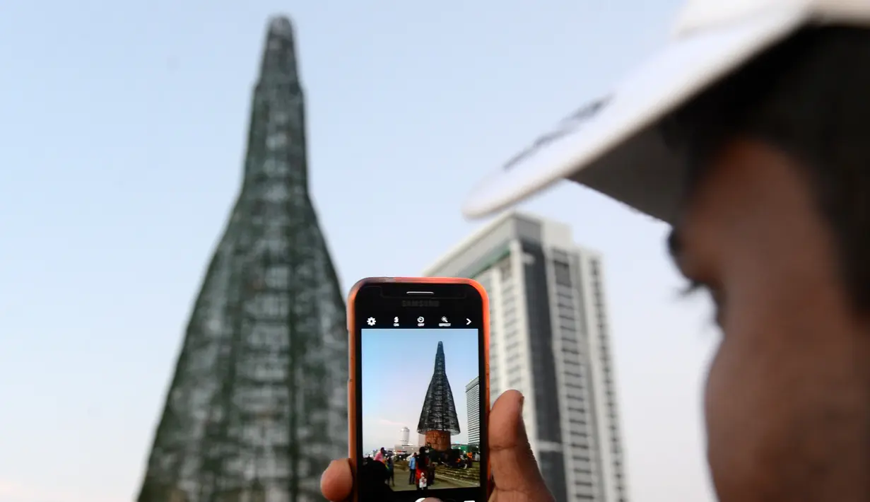 Seorang pria Sri Lanka mengambil foto pohon Natal di Kolombo, Sabtu (24/12). Tingginya yang mencapai 50 meter ini dinobatkan sebagai pohon natal tertinggi di dunia. (AFP PHOTO / Lakruwan Wanniarachchi)