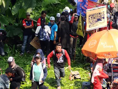 Massa buruh melintasi taman pembatas jalan di sekitar Kawasan Patung Patung Arjuna Wiwaha saat aksi perayaan hari Buruh Internasional 2017 di Jakarta, Senin (5/1). Ribuan massa buruh ikut turun ke jalan. (Liputan6.com/Helmi Fithriansyah)