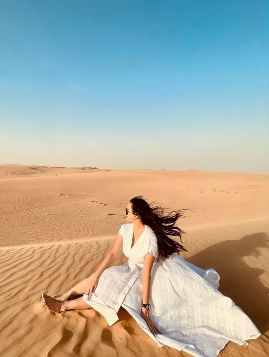 Aura Kasih berpose tak kalah menawan di tengah padang pasir. Ia mengenakan sebuah dress lengan pendek berwarna putih dan sunglasses. Potretnya semakin memukau karena rambut panjangnya yang dibiarkan tergerai tertiup angin. [Foto: Instagram/aurakasih]