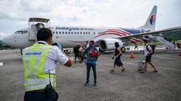 Petugas (kiri) membantu memotret penumpang setelah turun dari pesawat Boeing 738 Malaysia Airlines saat mendarat di Langkawi dari Bandara Internasional Kuala Lumpur (16/9/2021). Pulau liburan dibuka kembali untuk turis domestik setelah penutupan karena pembatasan Covid-19. (AFP/Mohd Rasfan)