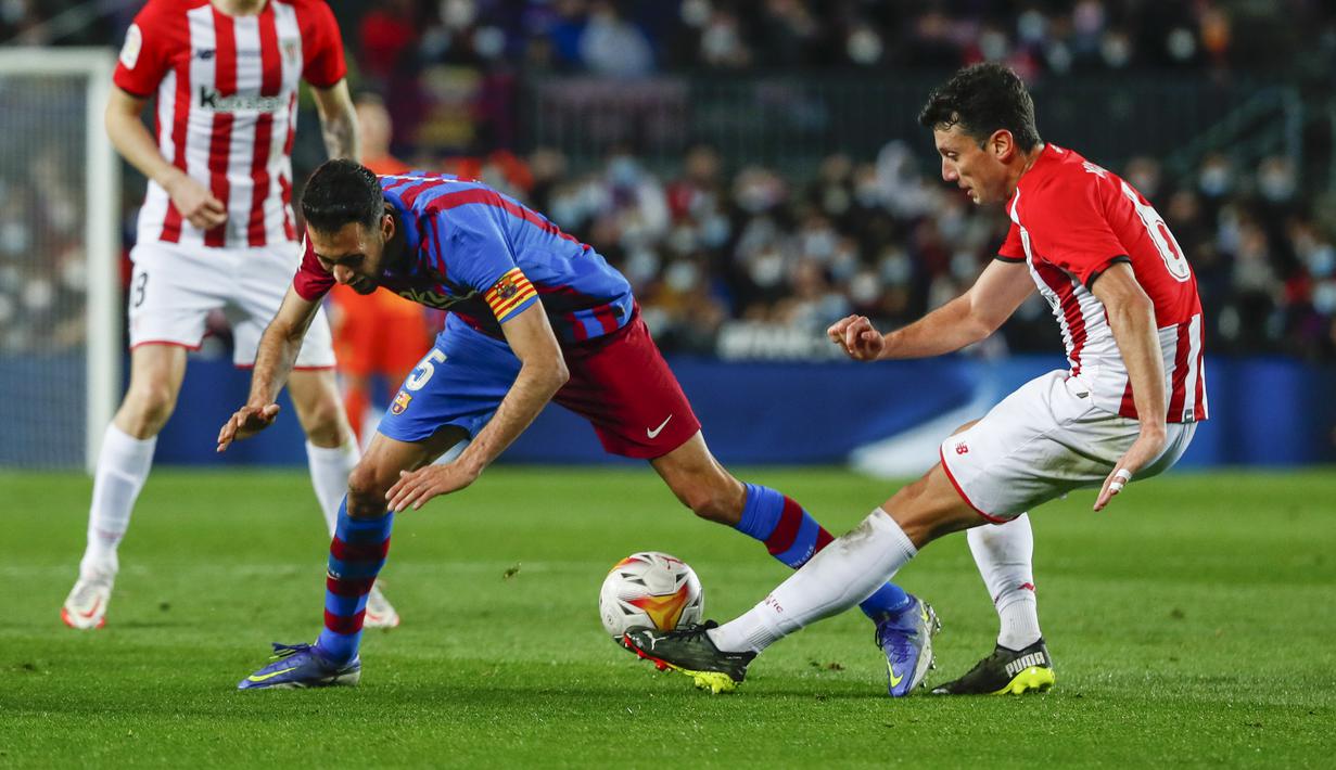 Gelandang Barcelona, Sergio Busquets (kiri) berebut bola dengan pemain Athletic Bilbao, Mikel Vesga selama pertandingan La Liga Spanyol di di stadion Camp Nou di Barcelona, Spanyol, Senin (28/2/2022). Dengan kemenangan ini Barcelona berada di posisi keempat dengan 45 poin.  (AP Photo/Joan Monfort)