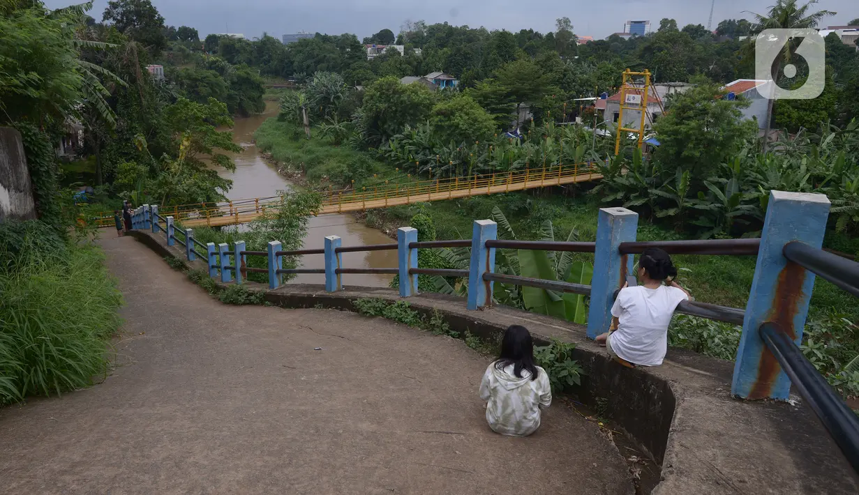 Anak-anak bersantai dekat jembatan gantung Kuning yang menghubungkan Pasar Minggu Poltangan ke Cililitan Condet, Jakarta, Selasa (28/12/2021). Jembatan gantung dengan panjang 40 meter di atas sungai Ciliwung tersebut baru baru ini dijadikan lokasi foto untuk konten medsos. (merdeka.com/Imam Buhori)