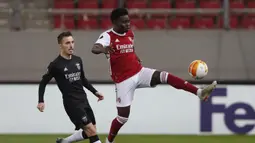 Striker Arsenal, Bukayo Saka (kanan) menguasai bola dibayangi bek Benfica, Alex Grimaldo dalam laga leg kedua babak 32 Besar Liga Europa 2020/21 di Georgios Karaiskakis Stadium, Kamis (25/2/2021). Arsenal menang 3-2 atas Benfica. (AP/Thanassis Stavrakis)