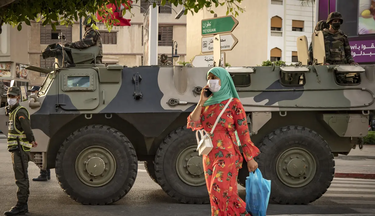 Seorang wanita berjalan saat tentara Maroko berpatroli di tengah wabah baru virus corona baru di kota Tangiers (11/8/2020). Tentara dikerahkan untuk meredam Lonjakan kasus Covid-19 di negara tersebut. (AFP/Fadel Senna)