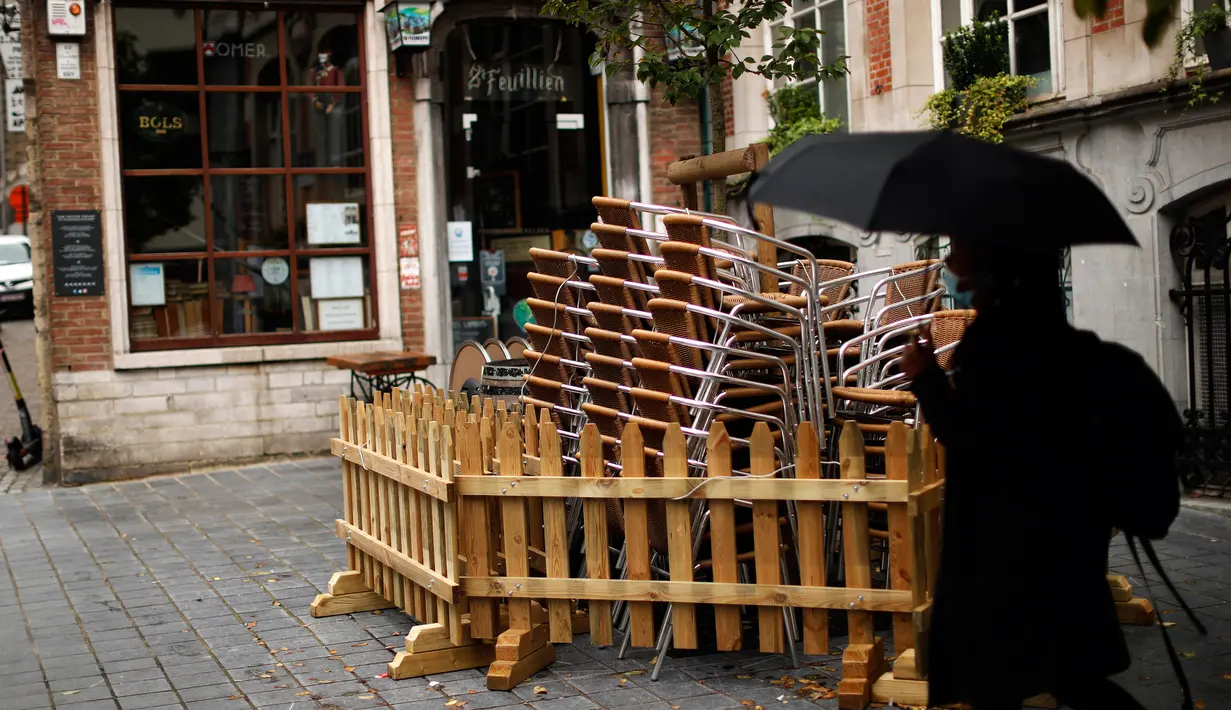 Seorang perempuan berjalan melewati tumpukan kursi dan meja dari bar yang tutup di Brussel, Belgia, Kamis (8/10/2020). Brussels pada Rabu, 7 Oktober 2020, memutuskan menutup semua bar, ruang dansa, dan kafetaria selama sebulan sebagai upaya membendung lonjakan COVID-19. (AP Photo/Francisco Seco)