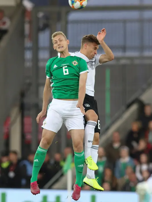 Bek Jerman, Joshua Kimmich (kanan) berebut bola udara dengan gelandang Irlandia Utara, George Saville saat kualifikasi Euro 2020 di Windsor Park, Belfast, Senin (9/9/2019). Jerman berhasil merebut puncak klasemen grup C kualifikasi Euro 2020 usai mengalahkan Irlandia Utara 2-0. (Paul Faith/AFP)