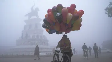 Seorang penjual balon berjalan di sepanjang jalan Heritage di tengah kabut tebal di hari yang dingin di Hari Tahun Baru, di Amritsar (1/1/2021). Gelombang Dingin, Kabut Tebal Mencengkeram India Utara di Hari Tahun Baru di Delhi. (AFP/Narinder Nanu)