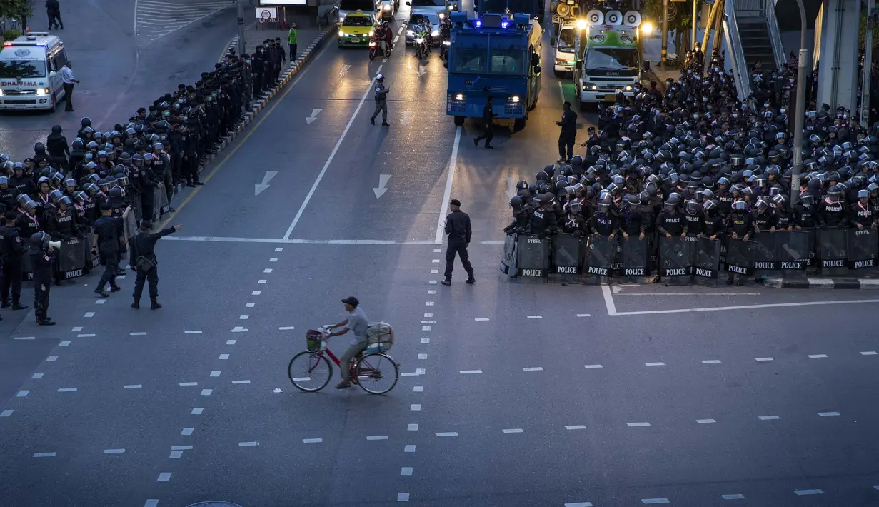 Seorang pria mengendarai sepedanya melewati polisi antihuru-hara yang mengambil posisi di persimpangan menuju Gedung Pemerintah setelah mengejar sekelompok kecil demonstran pro-demokrasi di Bangkok, Thailand, Kamis (15/10/2020). (AP Photo/Gemunu Amarasinghe)