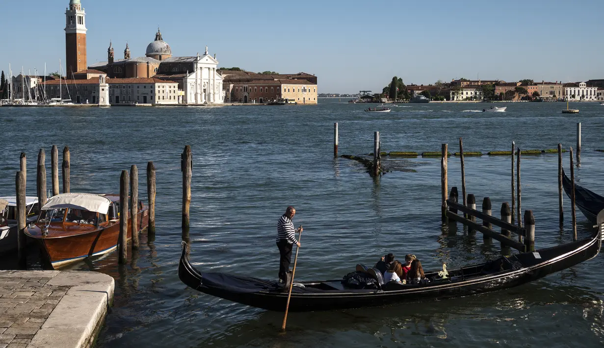 <p>Seorang gondolier mendayung gondola di dekat gereja Santa Maria della Salute di Venesia pada 20 Mei 2021. Turis kembali berdatangan menikmati keindahan Venesia, yang sering dijuluki kota paling romantis di dunia, setelah Italia menghapus kewajiban karantina bagi pendatang. (Marco Bertorello/AFP)</p>