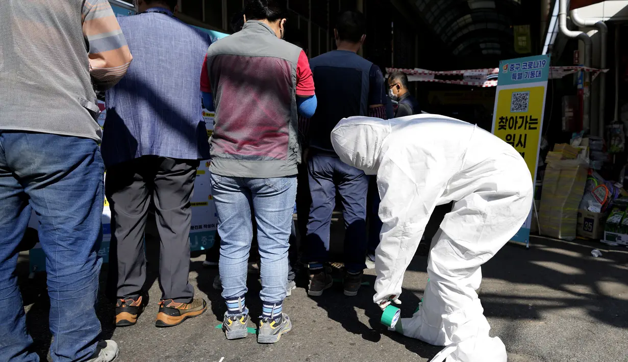 Seorang pekerja medis yang mengenakan alat pelindung menempelkan tanda-tanda untuk langkah-langkah jarak sosial dan tindakan pencegahan terhadap virus corona saat orang mengantre untuk menunggu untuk mendapatkan tes virus corona di Seoul, Korea Selatan, Jumat (24/9/2021). (AP Photo/Lee Jin-man)