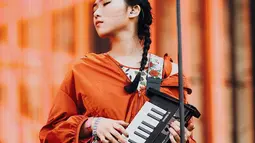 Penyanyi kelahiran tahun 1993 ini tampil dengan penuh penghayatan. Masih ditemani keyboard kesayangannya, dengan pakaian berwarna putih bercorak bunga-bunga dan outer berwarna oranye, ia tampak menawan dengan rambut dikepang (Liputan6.com/IG/@isyanasarasvati)
