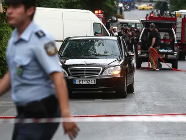 Seorang polisi berjalan dekat sebuah mobil di lokasi ledakan di pusat kota Athena, Kamis (25/5). Mantan PM Yunani, Lucas Papademos mengalami luka bakar di kaki dan tangannya akibat sebuah paket meledak di dalam mobil tersebut. (AP Photo/Yorgos Karahalis)