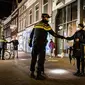 Polisi mengontrol sertifikasi keluar pada orang yang lewat saat jam malam dimulai di Haarlem, Belanda (23/1/2021). Belanda memasuki fase terberat dari pembatasan anti-virus Corona hingga saat ini. (AFP/ANP/Koen van Weel)