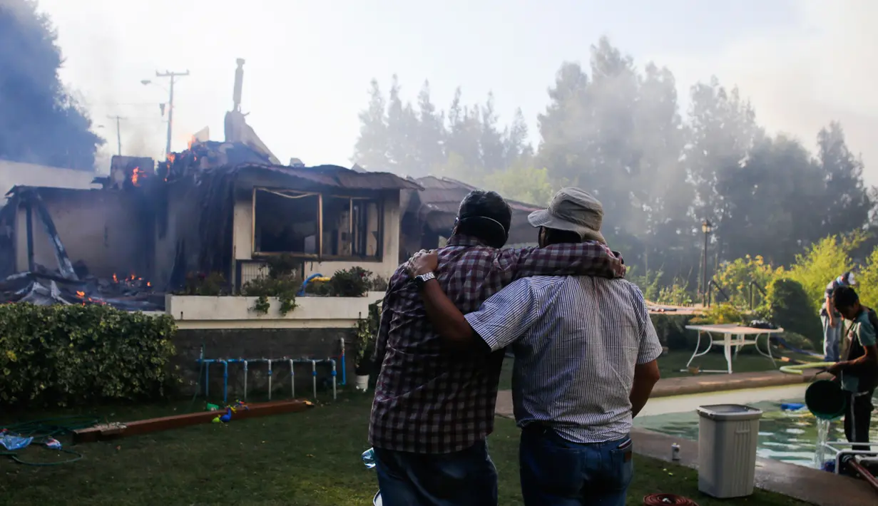 Dua orang pria menyaksikan sisa-sisa api yang membakar rumah mereka di Concepcion, Chili (26/1). Dalam peristiwa ini tidak ada korban jiwa. (Alejandro Zonez/Aton via AP)