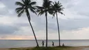 Orang-orang terlihat di samping tiga pohon kelapa di tepi pantai di pulau Phu Quoc selatan Vietnam (19/11/2021). Vietnam membuka kembali pulau resor Phu Quoc bagi pengunjung asing yang telah divaksinasi. (AFP/Nhac Nguyen)