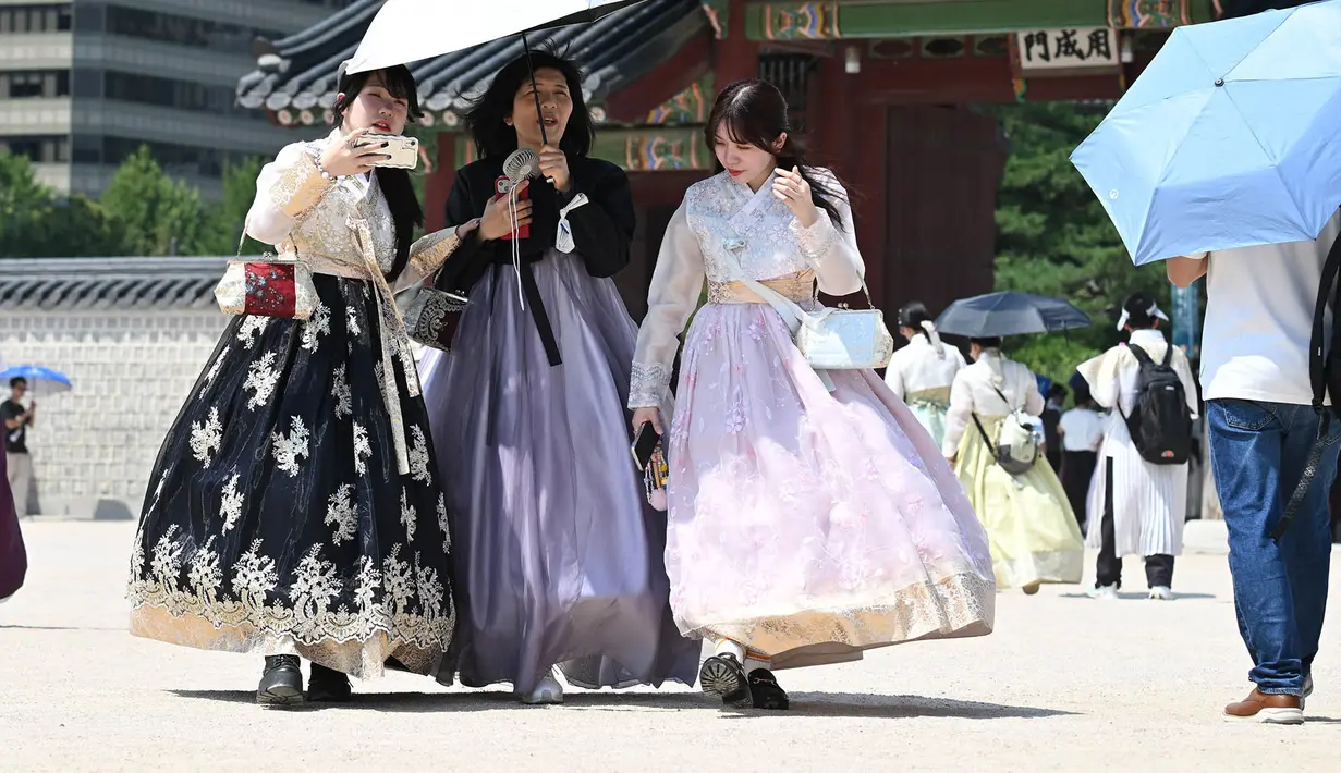 Para wisatawan yang mengenakan pakaian tradisional Hanbok menggunakan payung untuk melindungi diri dari terik matahari di Istana Gyeongbokgung di Seoul,  Korea Selatan, Senin,  3 Agustus 2026. (AFP/  Jung Yeon-je)
