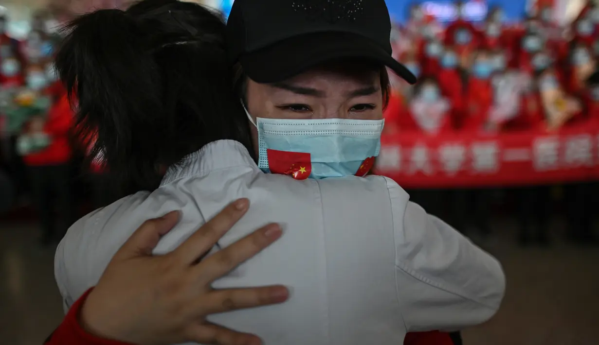Staf medis dari Provinsi Jilin (kanan) menangis ketika memeluk perawat dari Wuhan setelah bekerja bersama menangani pandemi Covid-19 selama upacara pelepasan di Bandara Tianhe, Wuhan, provinsi Hubei, Rabu (8/4/2020). Pemulangan itu bersamaan dengan dicabutnya lockdown Wuhan. (Hector RETAMAL/AFP)