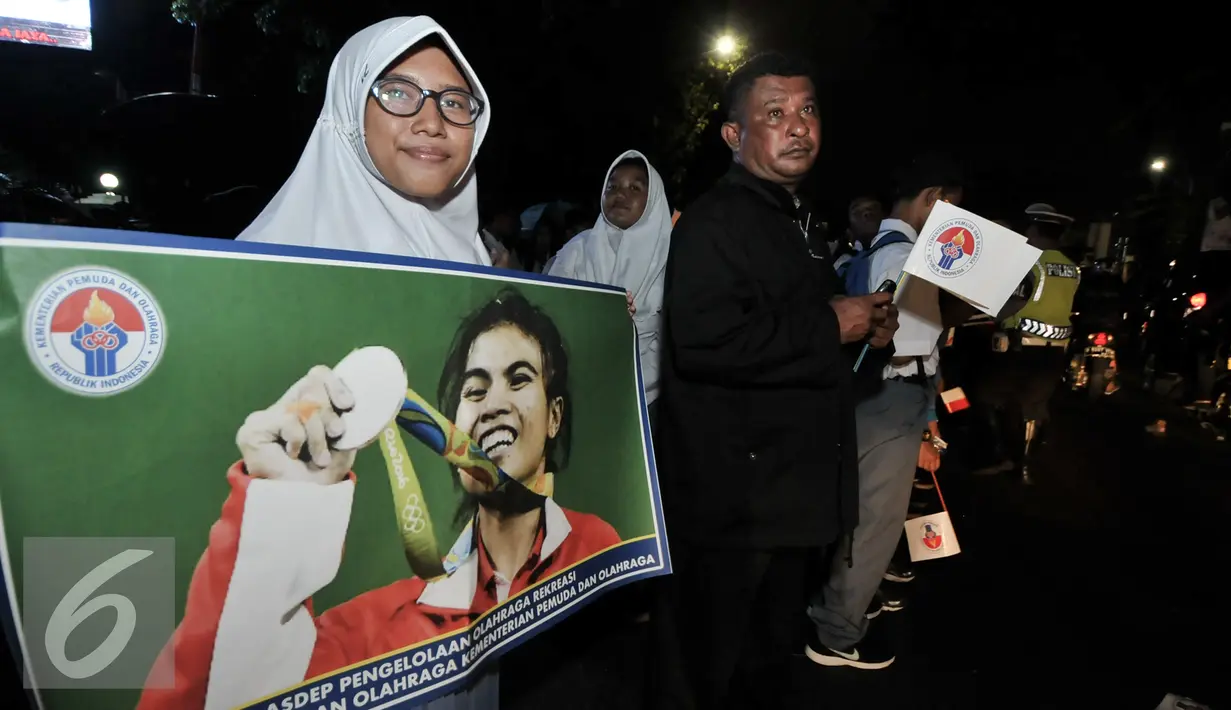 Seorang wanita membentangkan spanduk dengan gambar Sri Wahyuni peraih medali perak di Olimpiade Rio 2016, Jakarta, Selasa (23/8). Warga menyambut antusias kedatangan para atlet yang berlaga di Olimpiade Rio 2016. (Liputan6.com/Yoppy Renato)