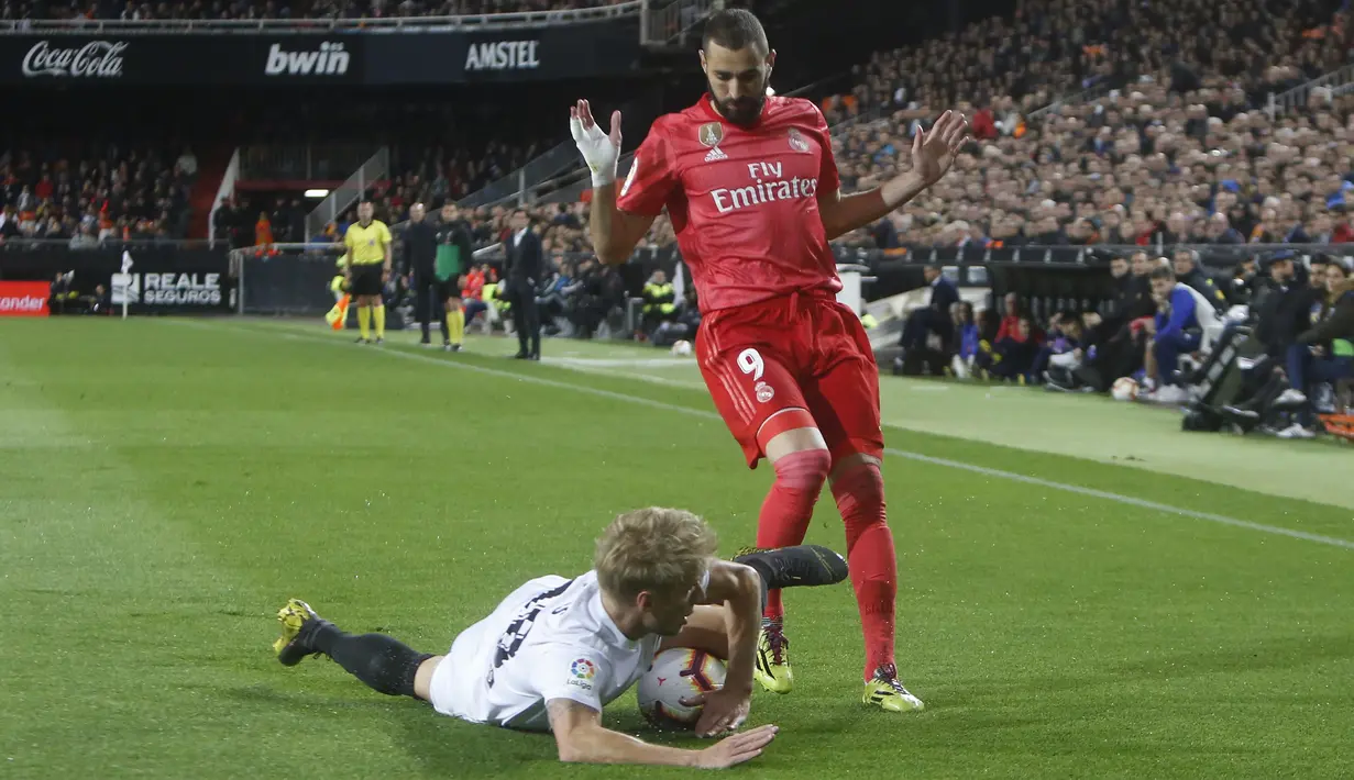 Pemain Valencia, Daniel Wass, terjatuh saat berebut bola dengan striker Real Madrid, Karim Benzema, pada laga La Liga 2019 di Stadion Mestalla, Rabu (3/4). Valencia menang 2-1 atas Real Madrid. (AP/Alberto Saiz)
