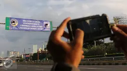 Seorang pengendara berhenti untuk mengambil gambar spanduk uji coba penghapusan kawasan 3 in 1 di jalan Gatot Subroto, Jakarta, Minggu (3/4/2016). Uji coba penghapusan kawasan 3 in 1 akan dilakukan pada hari selasa (5/4). (Liputan6.com/Herman Zakharia)