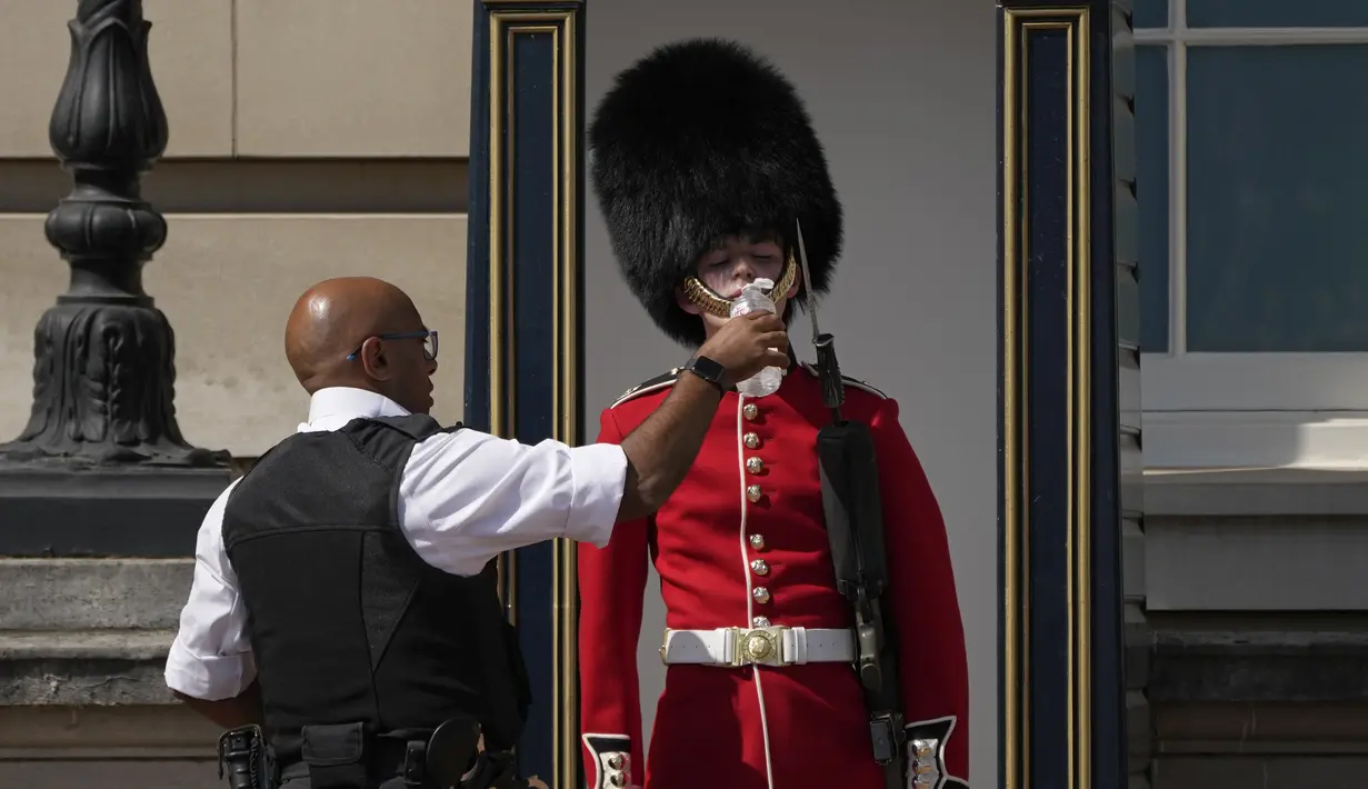 <p>Seorang anggota Pengawal Ratu di luar Istana Buckingham, menerima air minum dari petugas, saat cuaca panas melanda London, Senin (18/7/2022). Pemerintah Inggris telah mengeluarkan peringatan "merah" pertama mereka untuk panas ekstrem. (AP Photo/Matt Dunham)</p>