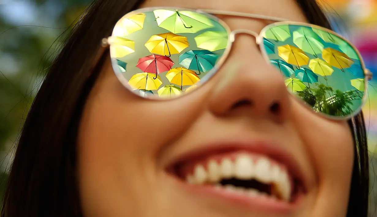 Kacamata pengunjung memantulkan payung warna-warni instalasi seni Umbrella Sky di Coral Gables, Florida, 16 Juli 2018. Proyek ini dikembangkan sebuah firma yang berdedikasi menciptakan instalasi perkotaan berkosep rendah biaya. (AP/Brynn Anderson)