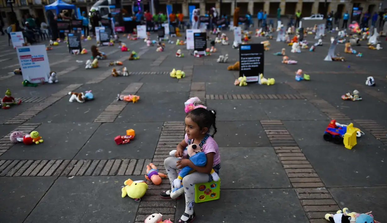 Seorang anak duduk bersama ratusan boneka saat menggelar aksi memprotes penganiayaan terhadap anak sekaligus meningkatkan kesadaran akan tanggung jawab dalam perlindungan anak di Alun-alun Bolivar, Bogota, Kolombia (20/11). (AFP Photo/Raul Arboleda)