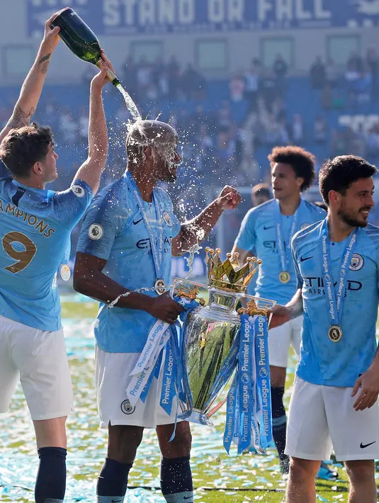 Pemain Manchester City John Stones menuangkan sampanye pada rekan setimnya Vincent Kompany yang memegang trofi Liga Inggris usai mengalahkan Brighton di Stadion AMEX, Brighton, Inggris, Minggu (12/5). (AP Photo/Frank Augstein)