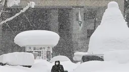 Seorang wanita berjalan di atas tumpukan salju di Toyama, di pesisir Laut Jepang, Senin (11/1/2021). Banyak yang tewas saat membersihkan salju ketika sistem udara dingin membuang hujan salju lebat di wilayah utara dan tengah negara itu. (Kyodo News via AP)
