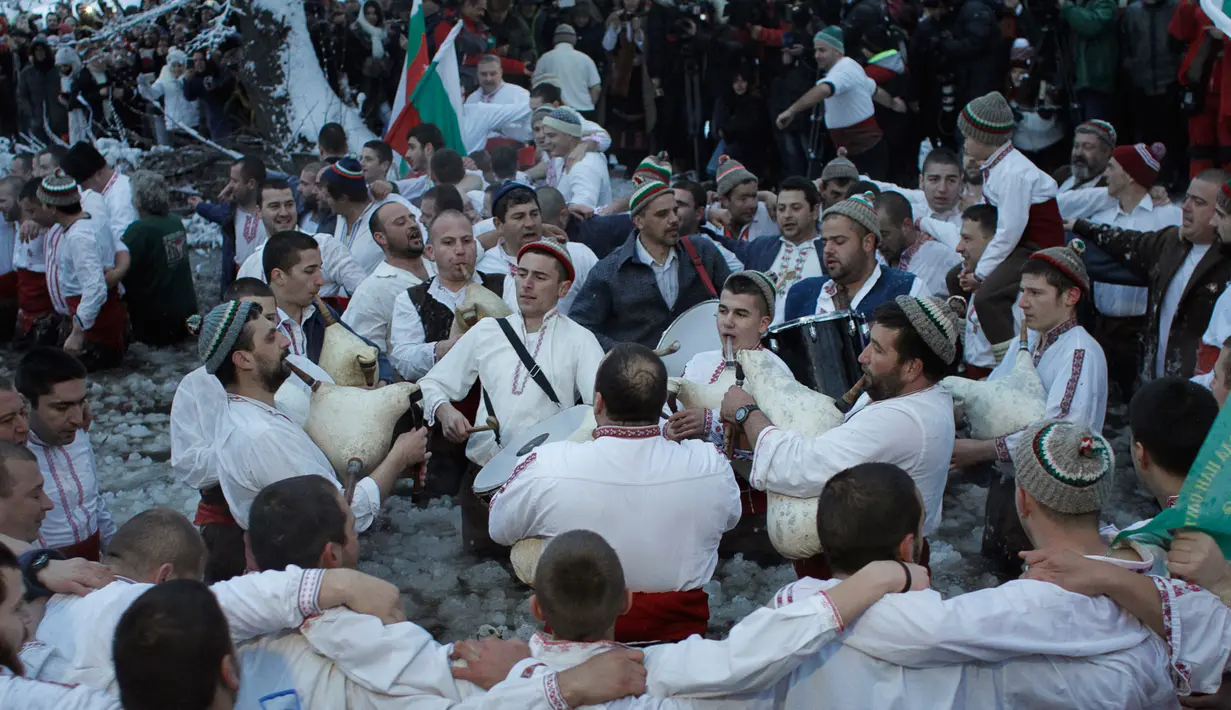 Sejumlah pria Bulgaria memainkan alat musik tradisional sambil menari di perairan sungai Tundzha selama Hari Epiphany di kota Kalofer, Bulgaria (6/1). Kegiatan ini juga dapat membawa kesehatan yang baik sepanjang tahun baru. (AP Photo/Valentina Petrova)