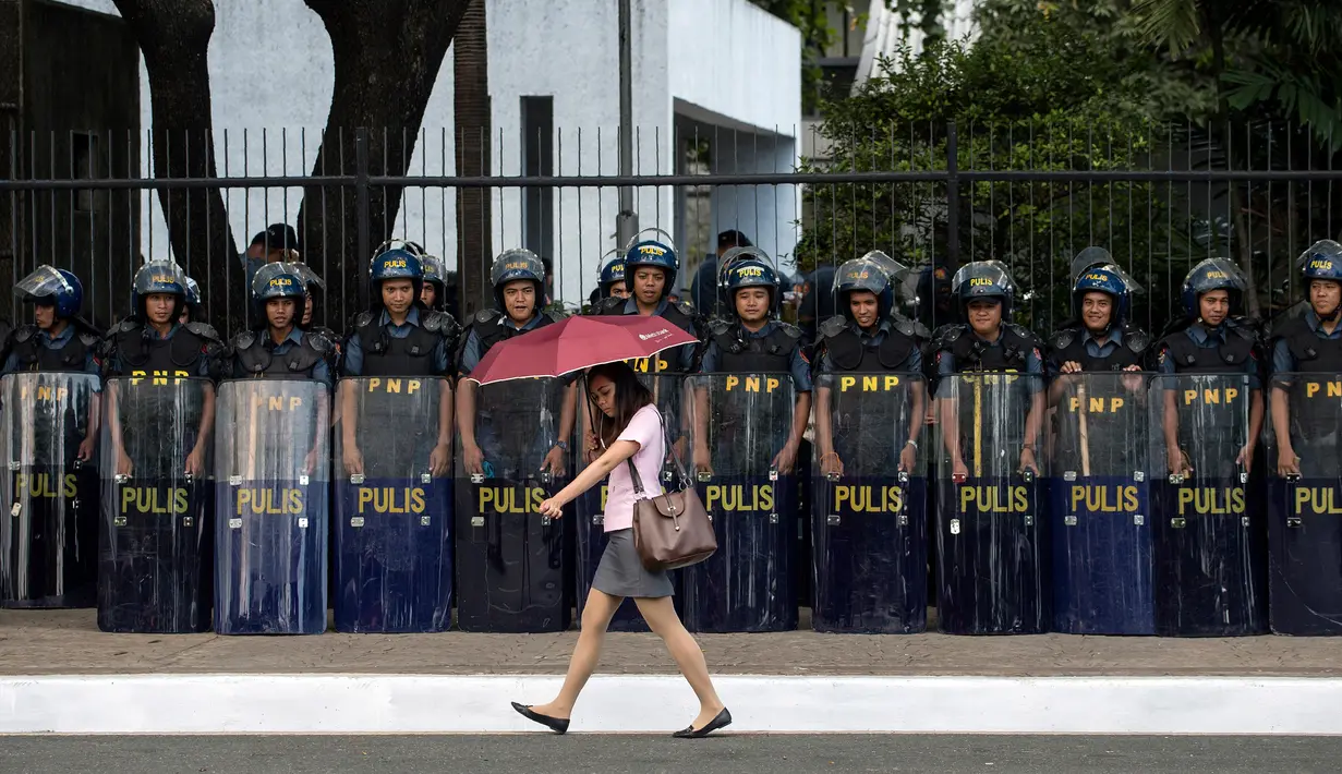 Seorang wanita melintas di dekat polisi yang berjaga di lokasi pertemuan ASEAN di Manila Bay, Filipina, Rabu (26/4). Sekitar 40 ribu pasukan keamanan dikerahkan untuk menjaga acara tersebut. (AFP PHOTO / Noel CELIS)