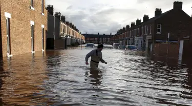 Seorang pria melintasi banjir yang merendam jalan pemukiman di Carlisle, Inggris, Minggu (6/12). Puluhan ribu rumah tidak punya listrik karena Badai Desmond yang menyebabkan banjir di Inggris utara dan sebagian Skotlandia. (REUTERS/Phil Noble)