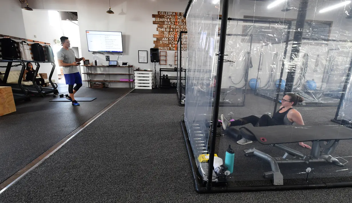 Peet Sapsin memimpin kelas dengan orang-orang berada dalam kotak plastik di Inspire South Bay Fitness di Redondo Beach, California pada 15 Juni 2020. Ruangan gym dengan plastik sebagai pemisah itu agar pengunjung dapat tetap berolahraga sambil tetap menjaga jarak fisik. (FREDERIC J. BROWN / AFP)