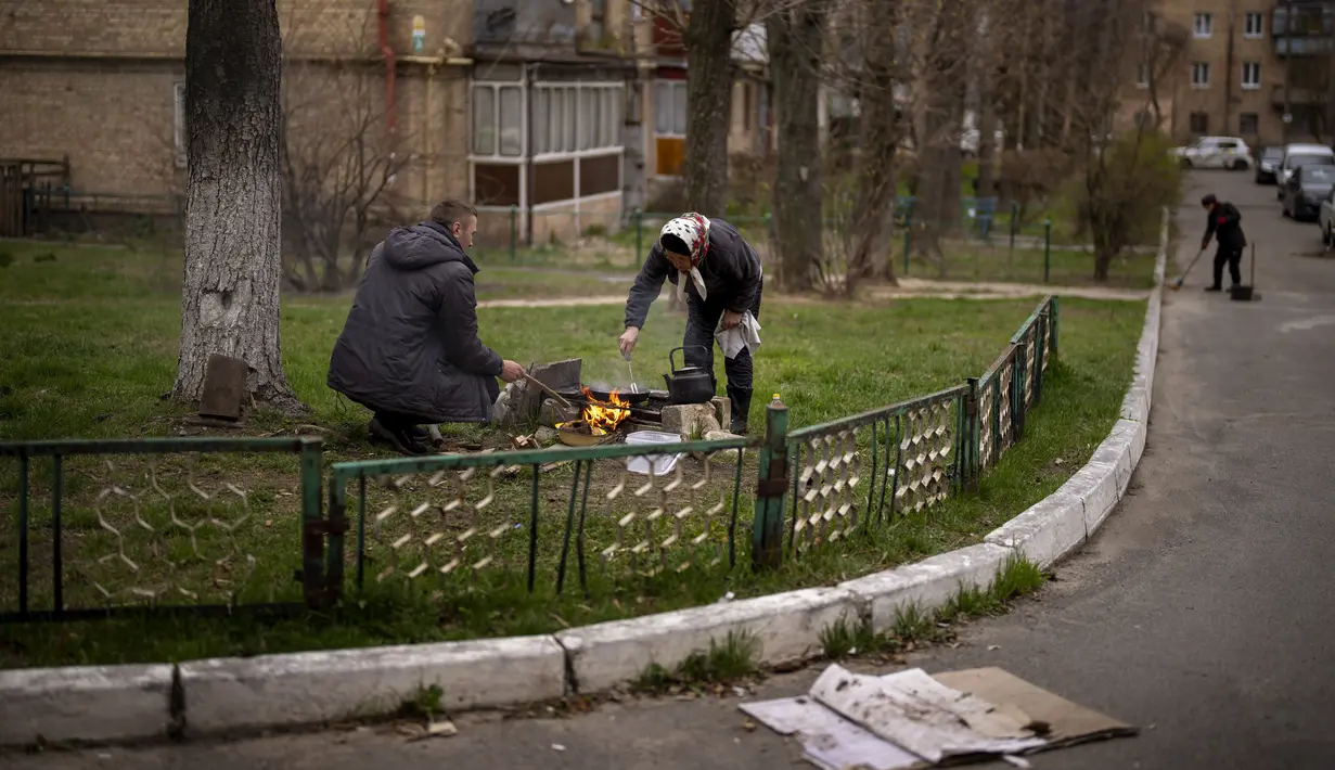Lyubov Lomachuk (69) memasak makan siang untuk keluarga dan tetangganya di atas api darurat di taman umum dekat rumahnya di Bucha, pinggiran Kiev, Senin (18/4/2022). Warga Bucha masih tanpa listrik, air dan gas setelah lebih dari 43 hari sejak invasi Rusia. (AP Photo/Emilio Morenatti)