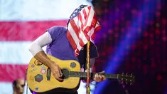 Vokalis grup band Coldplay, Chris Martin menutupi wajahnya dengan bendera Amerika Serikat sambil memainkan gitarnya saat menghibur para penonton di Lapangan FedEx di Landover, Md, AS (6/8). (Photo by Brent N. Clarke/Invision/AP)