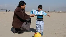 Murtaza Ahmadi (5), bocah asal Afghanistan, dibantu ayahnya memakai jersey yang ditandatangani langsung oleh bintang Barcelona, Lionel Messi, ketika bersiap main sepak bola di sebuah lapangan terbuka di Kabul, Jumat (26/2). (REUTERS/Omar Sobhani)