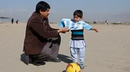 Murtaza Ahmadi (5), bocah asal Afghanistan, dibantu ayahnya memakai jersey yang ditandatangani langsung oleh bintang Barcelona, Lionel Messi, ketika bersiap main sepak bola di sebuah lapangan terbuka di Kabul, Jumat (26/2). (REUTERS/Omar Sobhani)