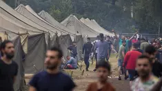 Para migran berjalan di dalam kamp pengungsi yang baru dibangun di tempat latihan militer Rudninkai, sekitar 38km (23,6 mil) selatan dari Vilnius, Lituania, Rabu (4/8/2021). (AP Photo/Mindaugas Kulbis)